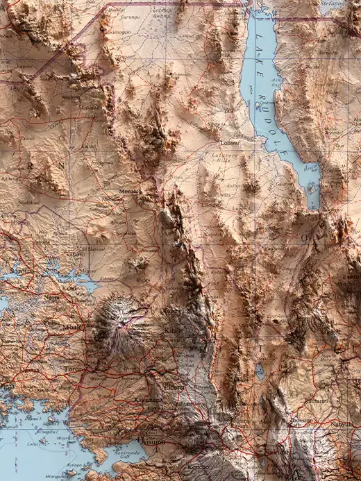 Topographic shaded relief map of the border region between Kenya and Uganda. The landscape features deep earthy tones and prominent shadows on mountain ridges like Mount Elgon, with the elongated, light-blue water body of Lake Rudolf (Lake Turkana) stretching across the upper right section